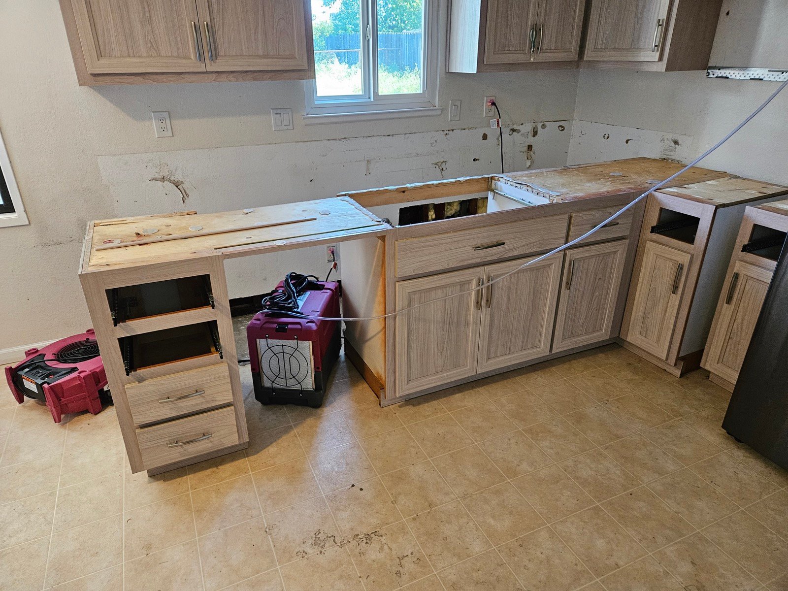 Lower kitchen cabinets detached from the wall with drying equipment behind them in Merced.