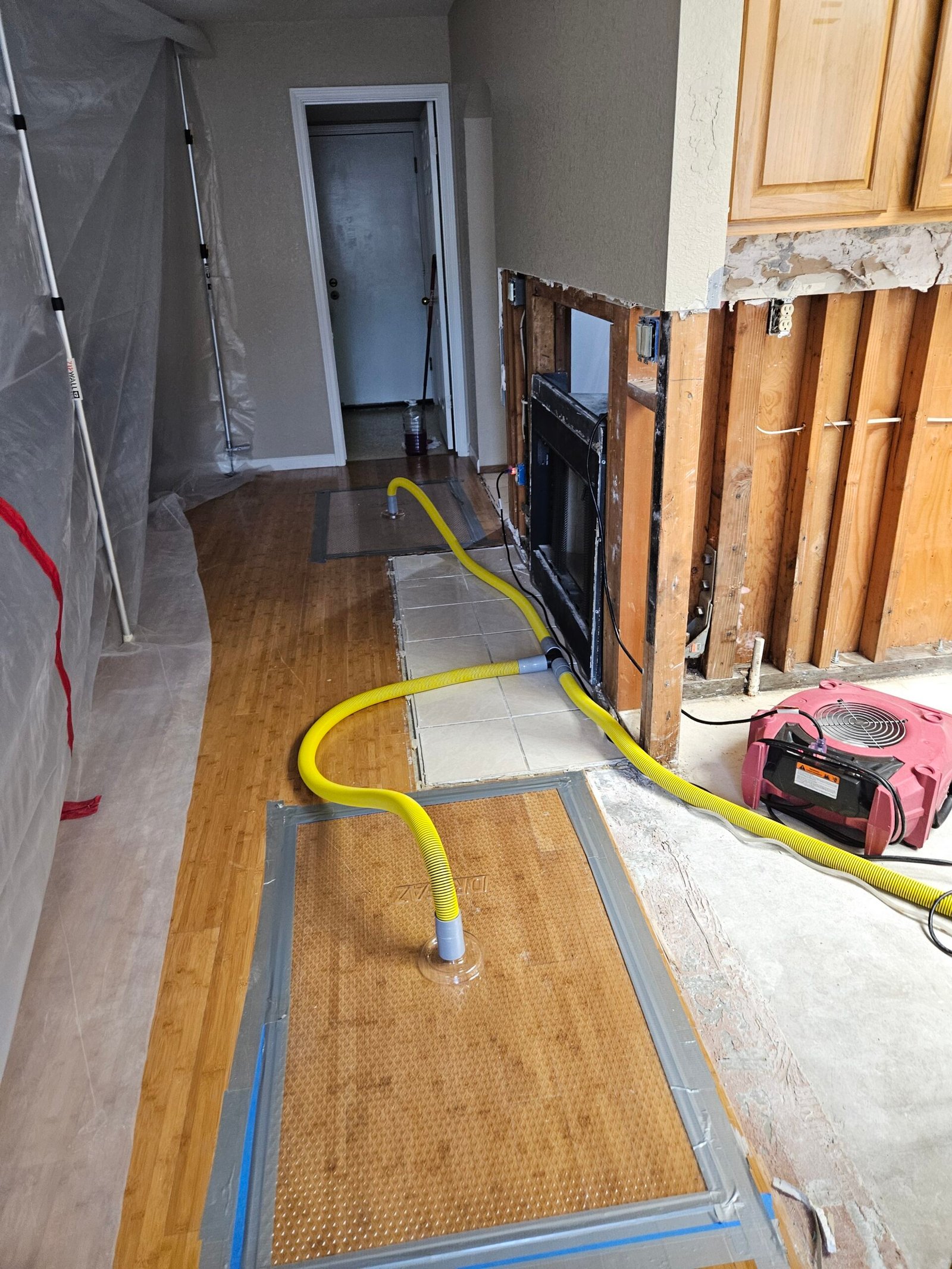 Floor-drying mats and yellow hoses on hardwood beside an opened kitchen wall in Stockton.