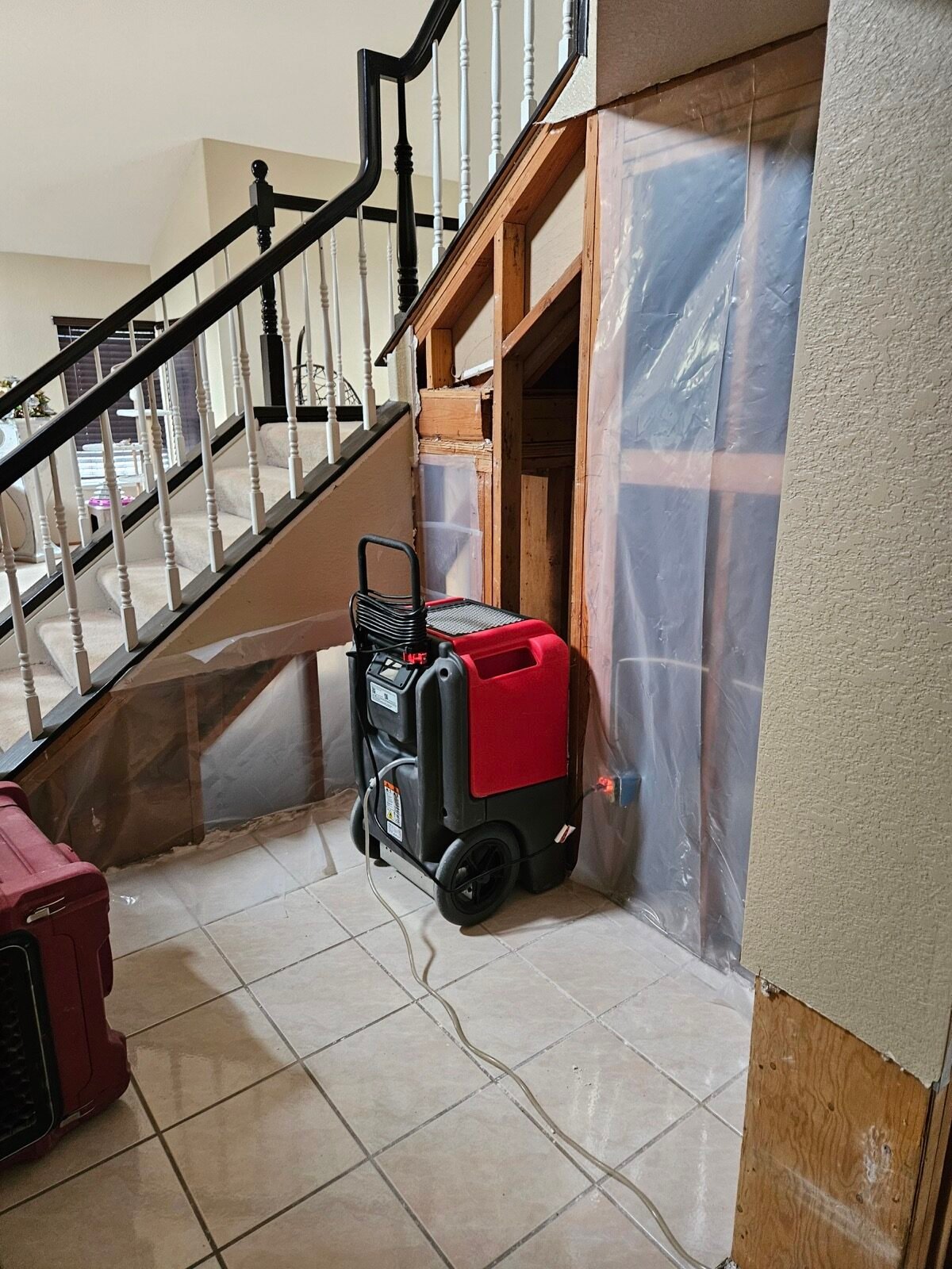 A dehumidifier beside exposed framing and containment near a staircase.